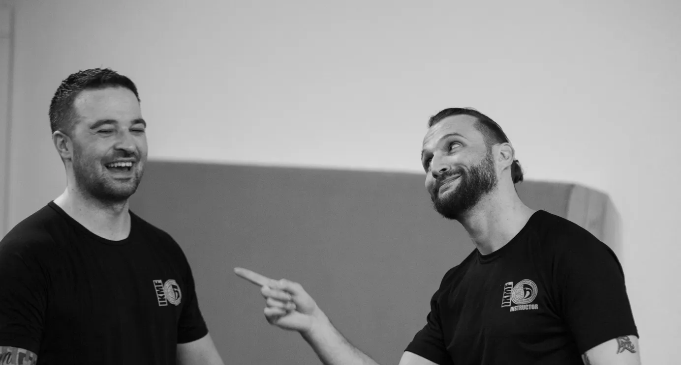 Two laughing instructors in IKMF shirts in the training room